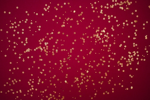 Photo Étoiles de paillettes d'or sur fond rouge foncé