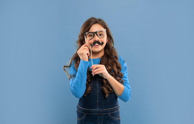 étonné fête adolescent fête temps anniversaire fête fête s'amuser laissez célébrer enfant avec les longs cheveux bouclés sur fond bleu enfant drôle avec des lunettes et moustache