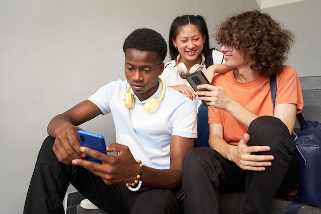 Un étudiant afro-américain discute seul et ses camarades de classe rient en utilisant leur téléphone portable