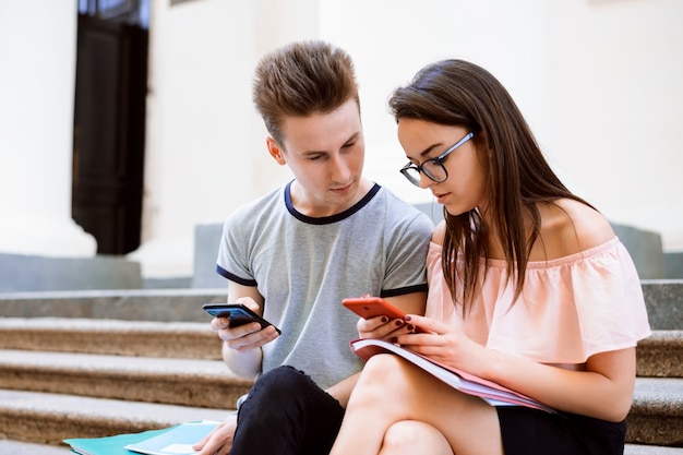 Un étudiant aide un ami à trouver des informations sur son téléphone portable alors qu'il était assis dans les escaliers du collège