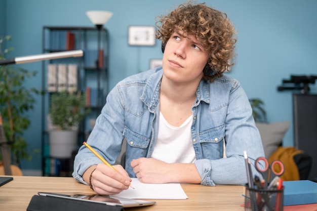 Un étudiant américain souriant du millénaire dans un casque assis au bureau pense à prendre des notes sur le webinaire