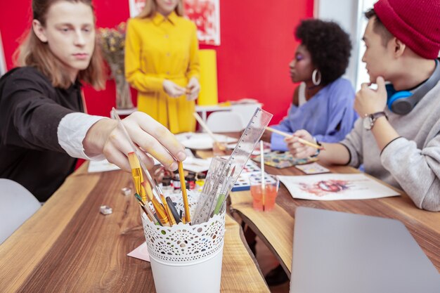 Étudiant En Art. Gros Plan D'étudiant En Art Aux Cheveux Blonds Portant Une Chemise Noire Et Blanche En Tenant Un Crayon