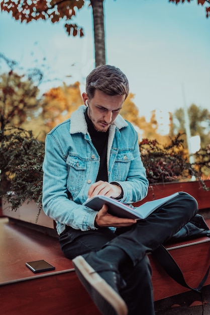 Un étudiant assis dans un parc devant l'université et lisant un livre