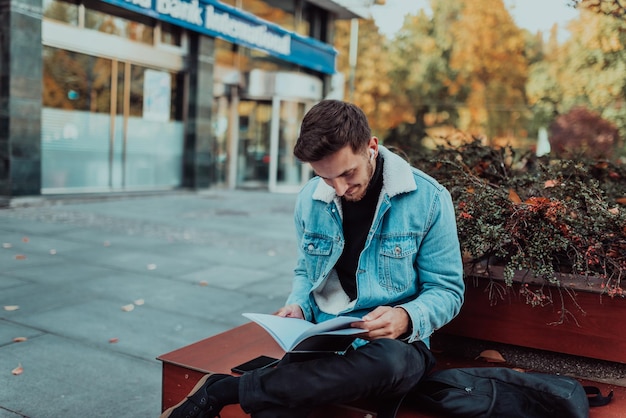 Un étudiant assis dans un parc devant l'université et lisant un livre