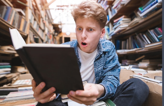 Un étudiant assis par terre dans une bibliothèque publique et passionné par la lecture d'un livre.