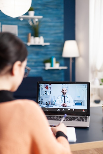 Photo Étudiant ayant une conférence vidéo en ligne avec un médecin consultant sur les traitements de santé. femme patiente utilisant un ordinateur portable pour une consultation médicale alors qu'elle était assise dans le salon