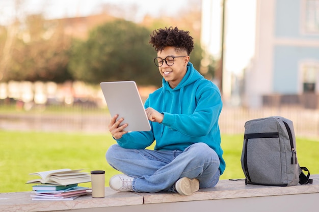 Un étudiant brésilien surfe sur une tablette numérique assis à l'extérieur.