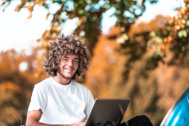 Un étudiant avec une coiffure afro assis dans la nature et utilise un ordinateur portable pendant une pandémie de virus corona. Photo de haute qualité