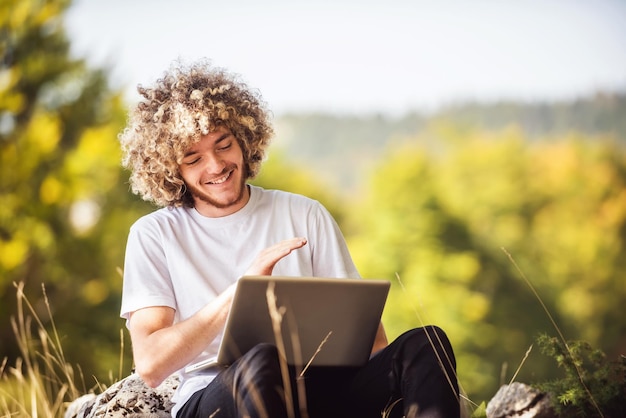 Un étudiant avec une coiffure afro assis dans la nature et utilise un ordinateur portable pendant une pandémie de virus corona. Photo de haute qualité