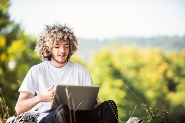 Un étudiant avec une coiffure afro assis dans la nature et utilise un ordinateur portable pendant une pandémie de virus corona