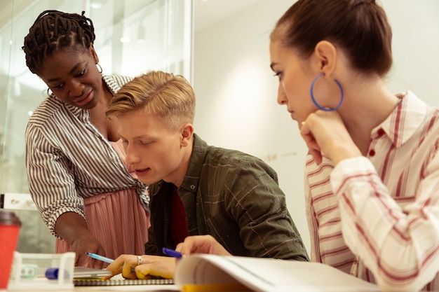 Photo Étudiant conscient. jeune homme concentré assis à la table tout en démontrant ses compétences linguistiques