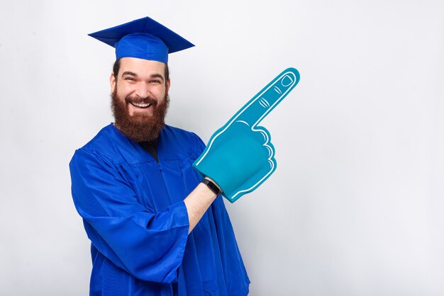 Un étudiant diplômé excité crie et porte un gant de fan pointant sur le fond.