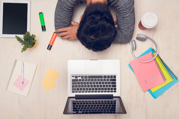 Un étudiant dort sur un bureau avec des livres autour. Vue de dessus