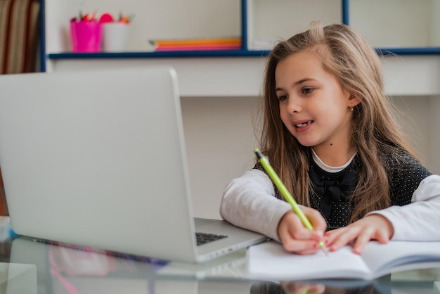 Un étudiant heureux qui écrit dans un cahier tout en apprenant pour l'école au bureau à domicile