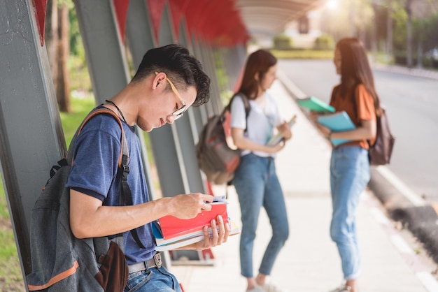 Un étudiant masculin lit sur le campus. Il y a des groupes d'amies derrière, concept d'éducation