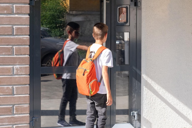 Un étudiant mignon avec un sac à dos scolaire ouvre la porte de la maison Un enfant rentrant chez lui après l'école à côté de la porte de la maison Concept de retour à l'école