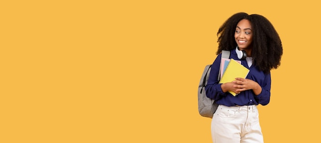 Un étudiant noir souriant avec des cahiers regardant de côté à l'espace libre sur un fond jaune