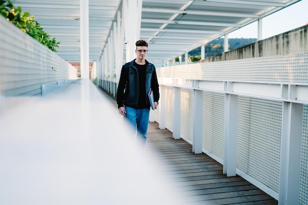 Étudiant portant des cahiers et marchant près d'une clôture en treillis