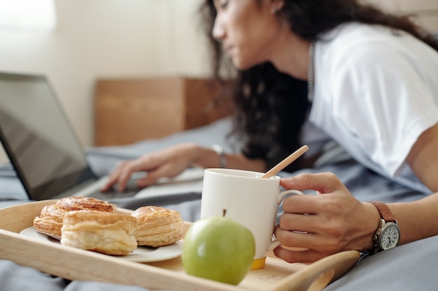 Photo Étudiant prenant une tasse de café avec de la pâtisserie fraîche et de la pomme pour le petit-déjeuner lors de la programmation sur un ordinateur portable