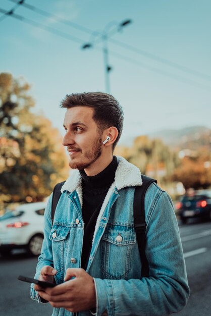 Un étudiant avec un sac à dos à l'aide d'un smartphone dans la rue vérifiant des messages électroniques et écoutant de la musique sur des écouteurs