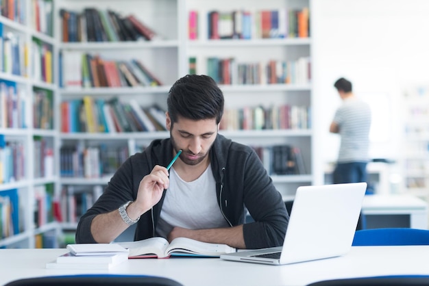 Photo Étudiant se préparant à un examen et apprenant des leçons dans la bibliothèque de l'école faisant des recherches sur un ordinateur portable et naviguant sur internet