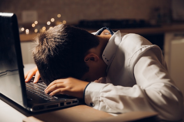 Photo l'étudiant se prépare à l'examen tard dans la nuit. un adolescent est assis devant un ordinateur portable et s'engage tard dans la soirée.