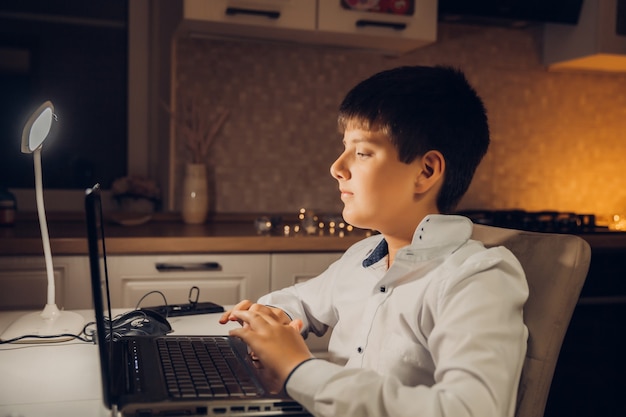 L'étudiant se prépare à l'examen tard dans la nuit. un adolescent est assis devant un ordinateur portable et s'engage tard dans la soirée.
