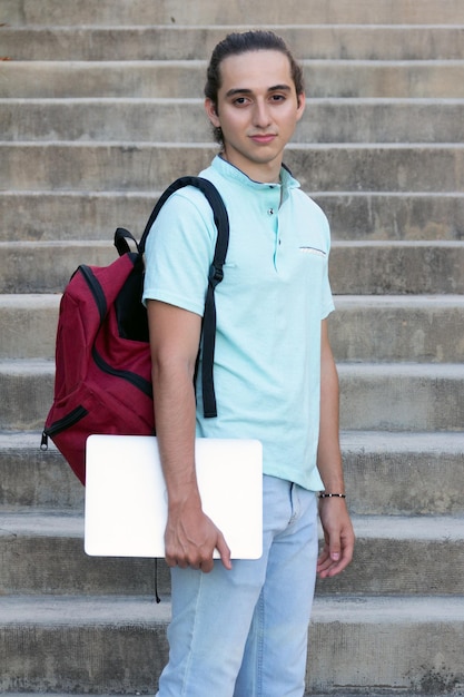 étudiant sérieux avec un ordinateur portable et un sac à dos en regardant la caméra