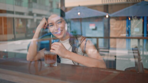 Étudiant souriant assis à la cafétéria avec vue sur le jus de verre à travers la fenêtre