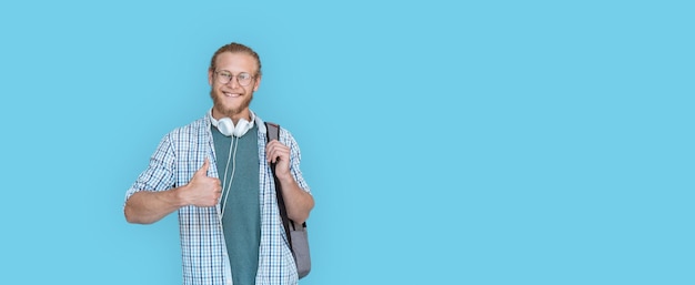 Un étudiant souriant tient son sac à dos et regarde la caméra isolée sur bleu