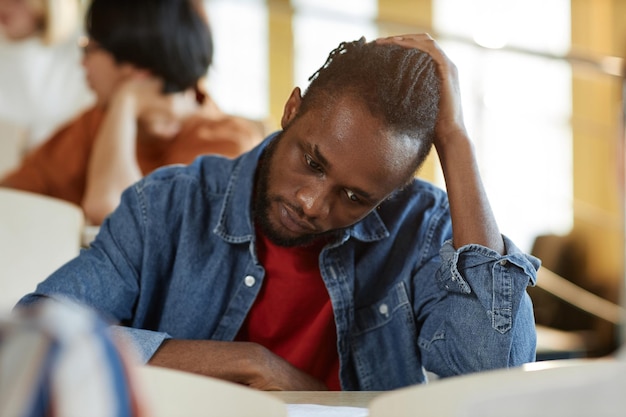 Étudiant stressé afro-américain assis au bureau en classe et examen d'écriture au collège