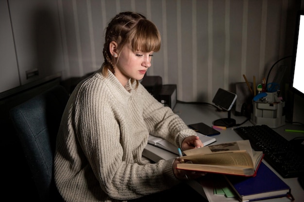 Un étudiant surmené est assis la nuit avec un livre Prendre des notes dans un cahier dans le noir