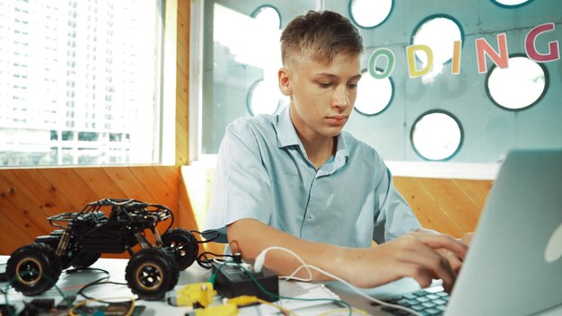 Photo Étudiant travaillant sur un ordinateur portable tout en analysant la construction d'un modèle de voiture