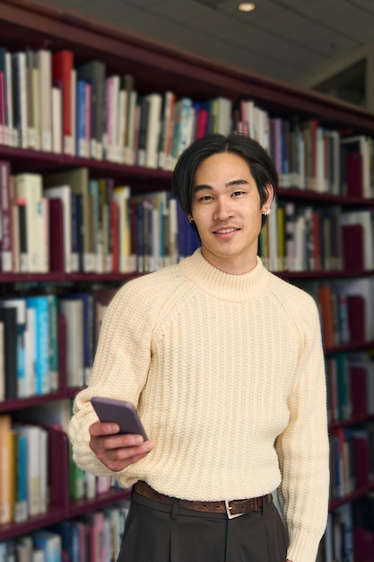 Un étudiant universitaire japonais intelligent tenant un téléphone portable dans le concept d'éducation moderne de la bibliothèque