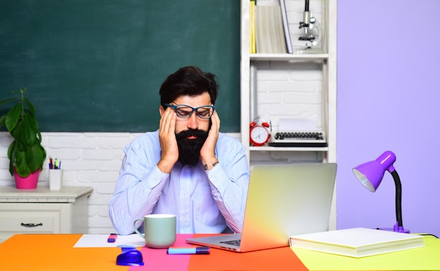 Étudiant universitaire masculin fatigué à l'intérieur d'un professeur barbu près d'un tableau dans le professeur de classe de l'école