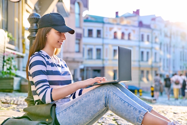 Étudiante adolescente utilisant un ordinateur portable à l'extérieur assise sur le trottoir arrière-plan urbain Éducation technologique mode de vie adolescent concept de jeunesse