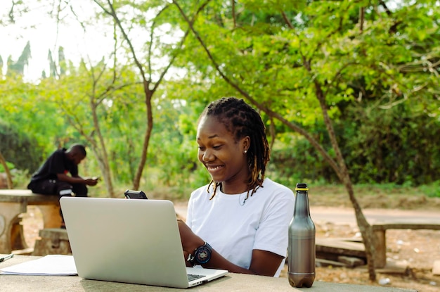 Une étudiante africaine adolescente envoie des SMS avec un téléphone portable et un ordinateur portable