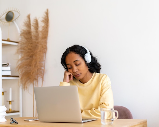 Étudiante afro-américaine ennuyée dormant pendant des cours en ligne sur un ordinateur portable à la maison