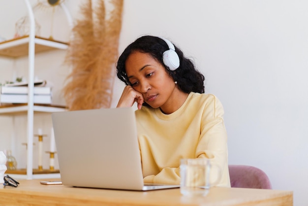 Photo Étudiante afro-américaine ennuyée et fatiguée regardant un cours à distance en ligne sur un ordinateur portable