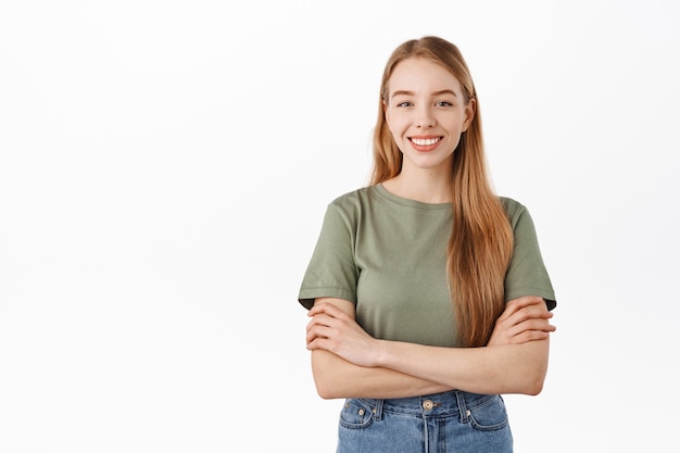 Une étudiante a l'air heureuse à l'avant dans des vêtements décontractés, debout sur un mur blanc