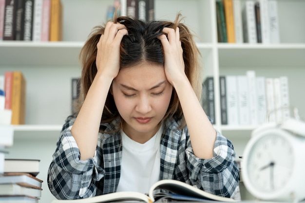 L'étudiante asiatique a de l'anxiété à cause des examens. La femme se prépare pour le test et apprend des leçons à la bibliothèque. Le stress, le désespoir, la précipitation, l'incompréhension, la lecture, les attentes, la connaissance.