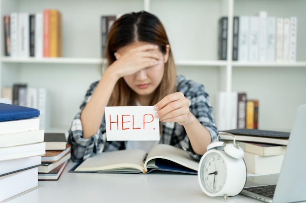 Une étudiante asiatique est anxieuse à cause des examens. Une femme se prépare aux tests et aux leçons d'apprentissage dans la bibliothèque. Stress, désespoir, hâte, incompréhension, lecture, attentes découragées, connaissances.