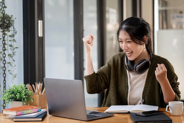 Une étudiante asiatique excitée se sent euphorique en célébrant le résultat de la réussite de la victoire en ligne via un ordinateur portable