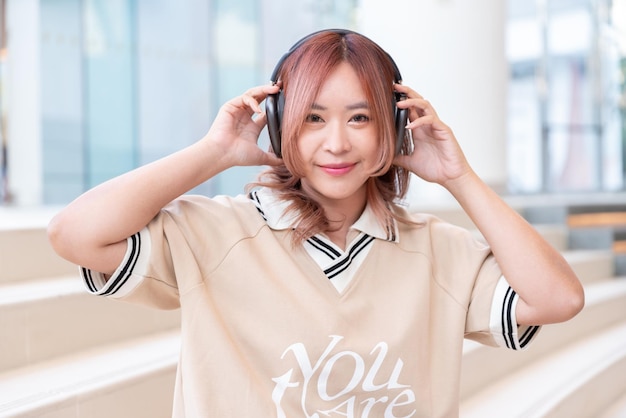 Photo une étudiante asiatique heureuse écoute de la musique sur un casque dans la bibliothèque du campus de l'université