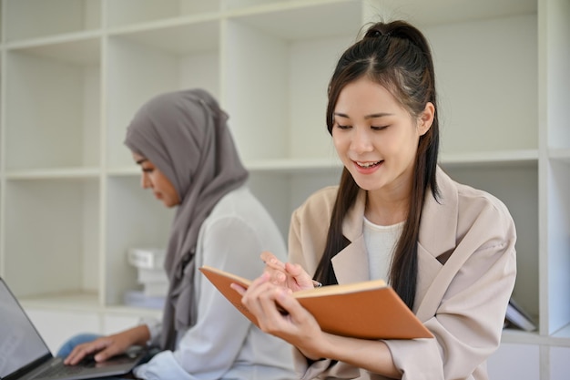 Une étudiante asiatique lit un livre dans l'espace de coworking de la bibliothèque du campus