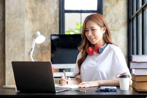 Une étudiante asiatique utilisant un ordinateur portable qu'elle étudie en ligne, elle regarde l'ordinateur portable en écoutant attentivement ce que l'enseignant enseigne Concept d'apprentissage en ligne