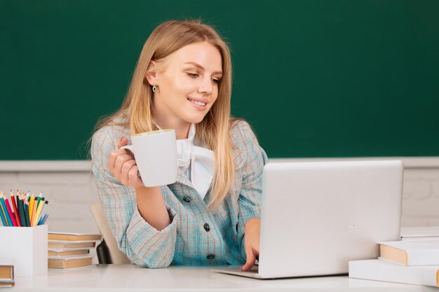 Une étudiante buvant du café ou du thé travaillant sur un ordinateur portable en classe se préparant à un examen