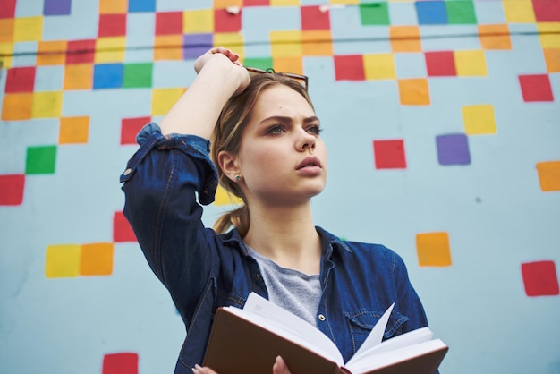 Une étudiante en chemise et lunettes tient un livre dans ses mains dans la rue près du graffiti sur le mur photo de haute qualité