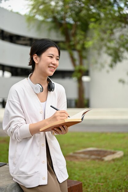 Une étudiante dans un cardigan confortable est assise à une table dans le parc du campus et écrit son journal