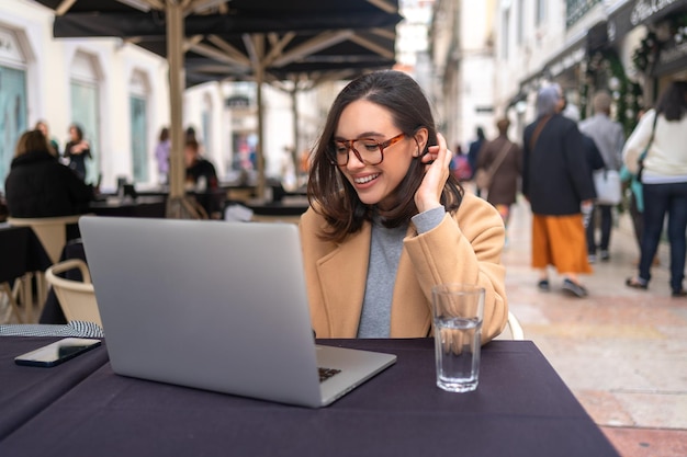 Une étudiante enthousiaste, heureuse et insouciante prépare un projet indépendant assise dans un café en plein air.